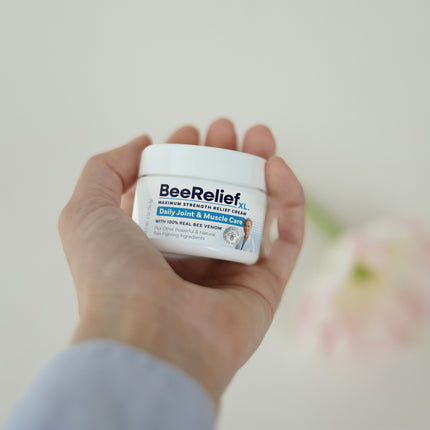 Hand holding a jar of BeeRelief XL cream against a light background